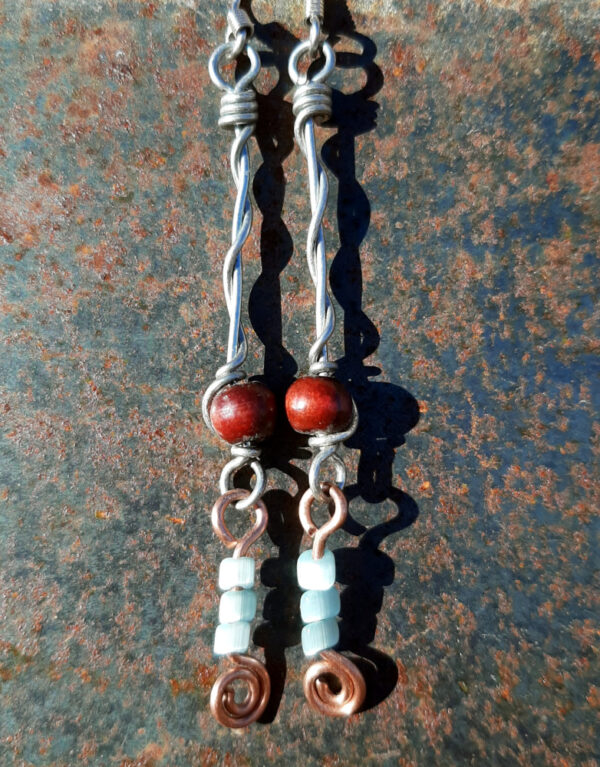 Each earring has two sections. The lower has three pale blue beads strung on copper wire with a neat spiral at the bottom. This is linked to a piece with a round red wooden bead strung on steel wire that curves back up around the bead, then twists around itself.