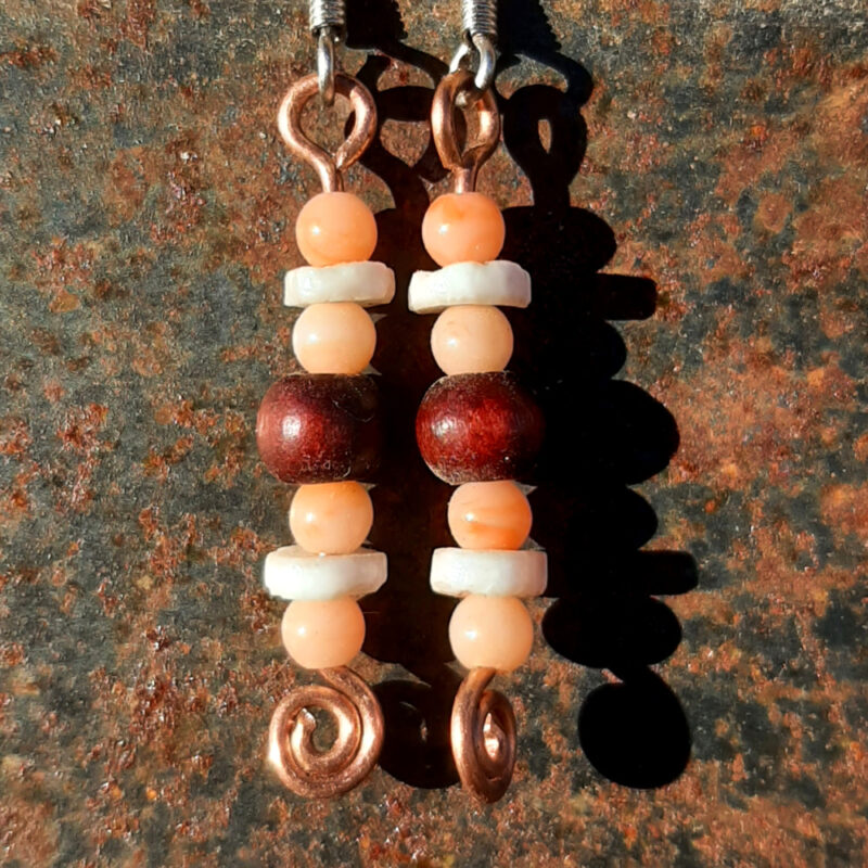 Each earring has a disc-shaped bone bead between two round peach-colored beads. below them is a round red wooden bead, and below that, another set of the peach and bone beads. All are strung on copper wire that ends at the bottom in a neat spiral.