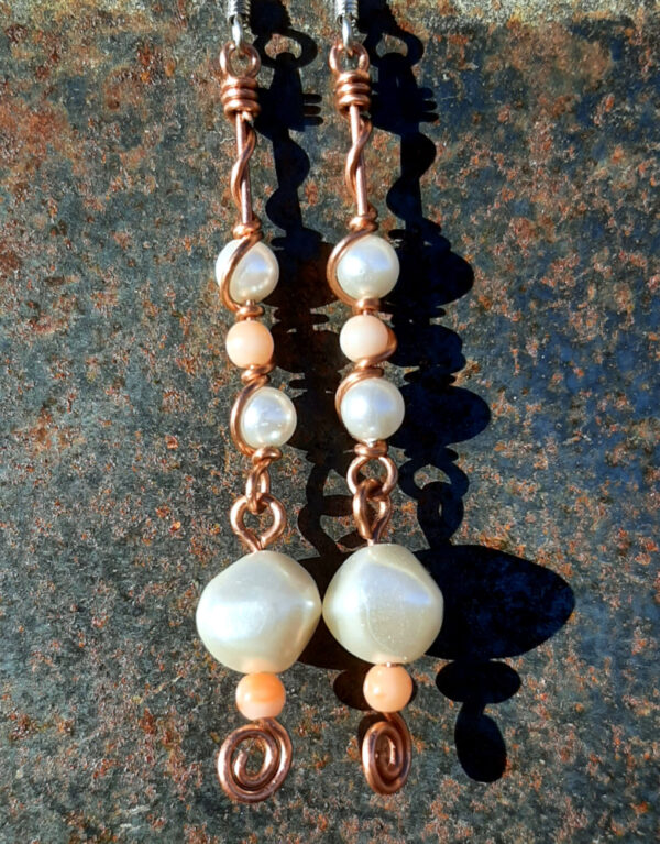 Each earring has two sections. The lower has a round white bead with a much smaller peach bead below it, both strung on copper wire with a neat spiral at the bottom. This is linked to a piece with another peach bead between two white beads, all strung on copper wire that curves back up around the beads, then twists around itself.