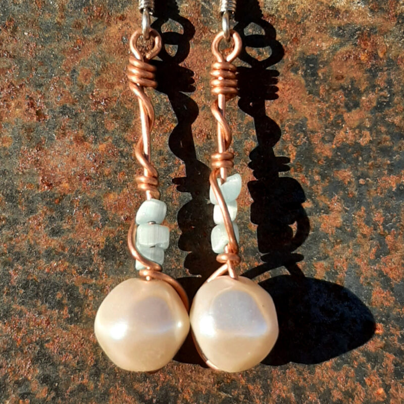 Each earring has a round white bead with three smaller pale blue beads above it, all strung on copper wire that curves back up around each bead, then twists around itself.