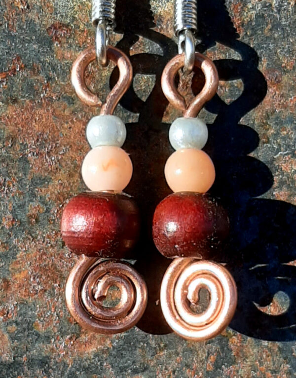 Each earring has a tiny round pale blue bead, then a slightly larger peach bead, and below those a round red wooden bead. All are strung on copper wire that ends at the bottom in a neat spiral.