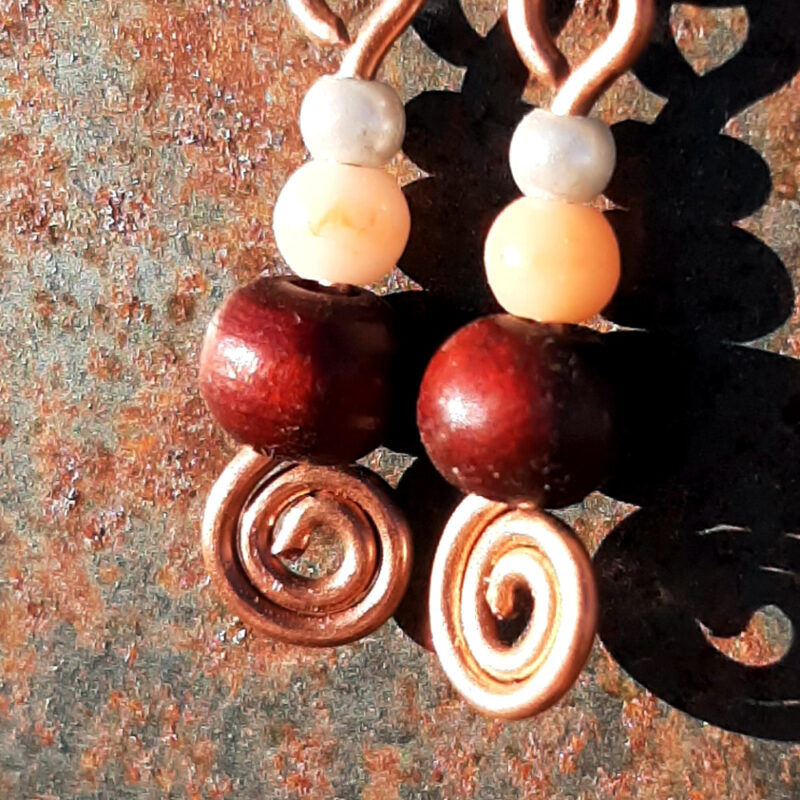 Each earring has a tiny round pale blue bead, then a slightly larger peach bead, and below those a round red wooden bead. All are strung on copper wire that ends at the bottom in a neat spiral.