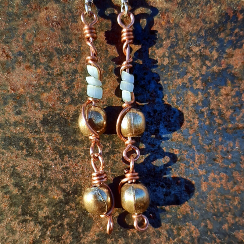 Each earring has two sections. The lower has a round brass bead strung on copper wire with a neat loop at the bottom. This is linked to a piece with another brass bead with three pale blue beads above it, all strung on copper wire that curves back up around the beads, then twists around itself.