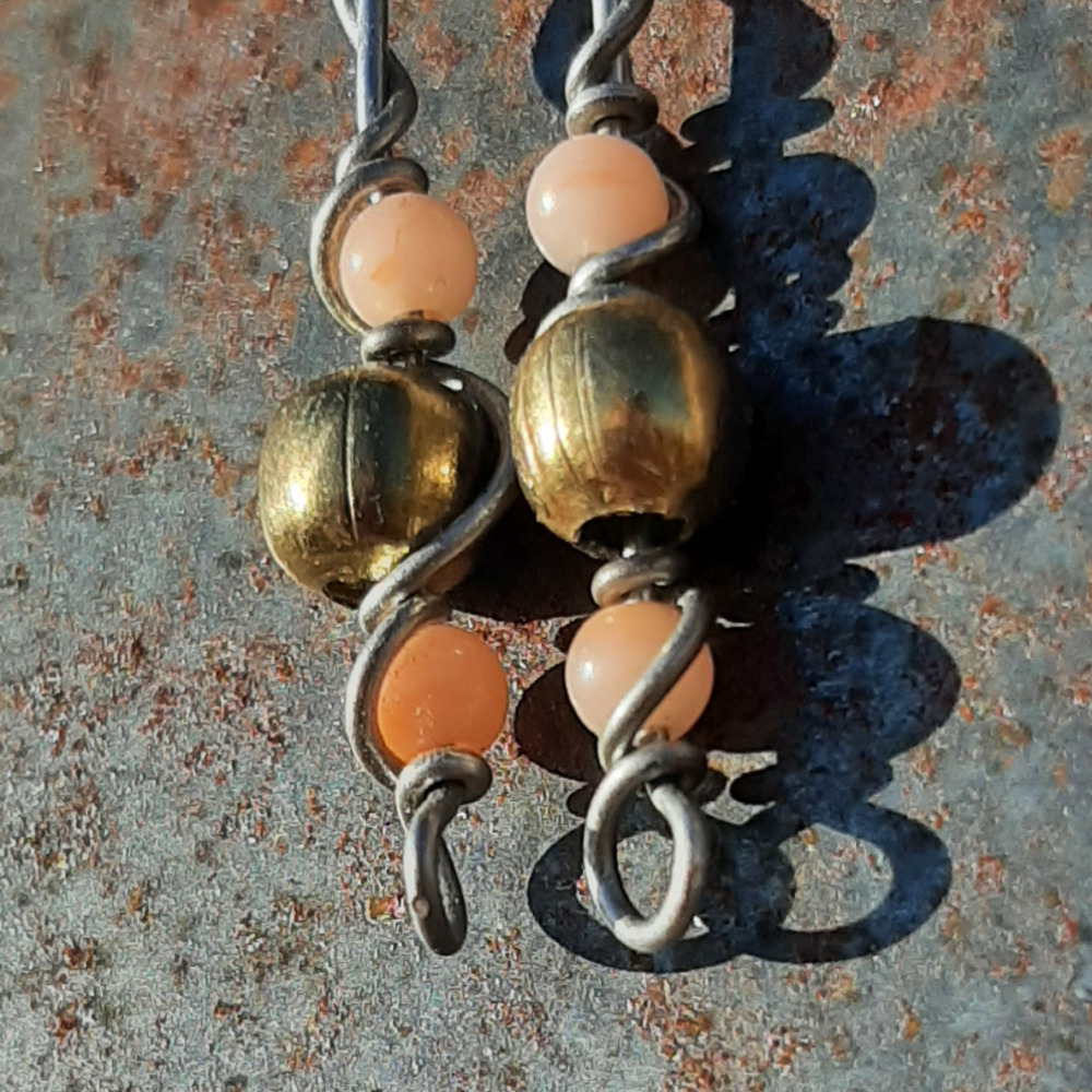 Each earring has a round brass bead with smaller peach beads above and below, all strung on steel wire that curves back up around each bead, then twists around itself.