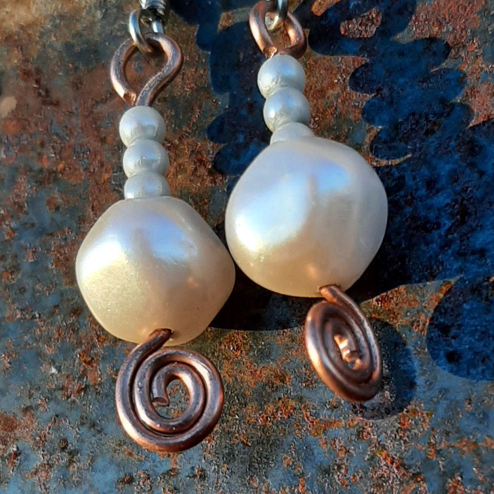 Each earring has a round white bead below three round pale blue beads. All are strung on copper wire that ends at the bottom in a neat spiral.