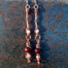 Each earring has two sections. The lower has a round red wooden bead with a slightly smaller peach bead below it, both strung on copper wire with a neat loop at the bottom. This is linked to a piece with another peach bead strung on copper wire that curves back up around the beads, then twists around itself.