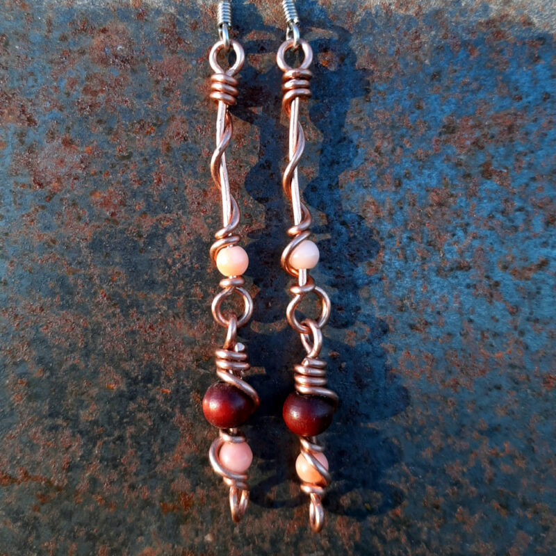 Each earring has two sections. The lower has a round red wooden bead with a slightly smaller peach bead below it, both strung on copper wire with a neat loop at the bottom. This is linked to a piece with another peach bead strung on copper wire that curves back up around the beads, then twists around itself.