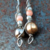 Each earring has a round brass bead at the bottom, with two smaller pale blue beads surrounding a peach bead above it, all strung on steel wire that curves back up around each bead, then twists around itself.