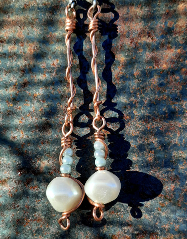 Copper wire earrings, hinged at the middle; at the top, copper wire wrapping around itself; below, a single white bead with three tiny pale blue beads above.