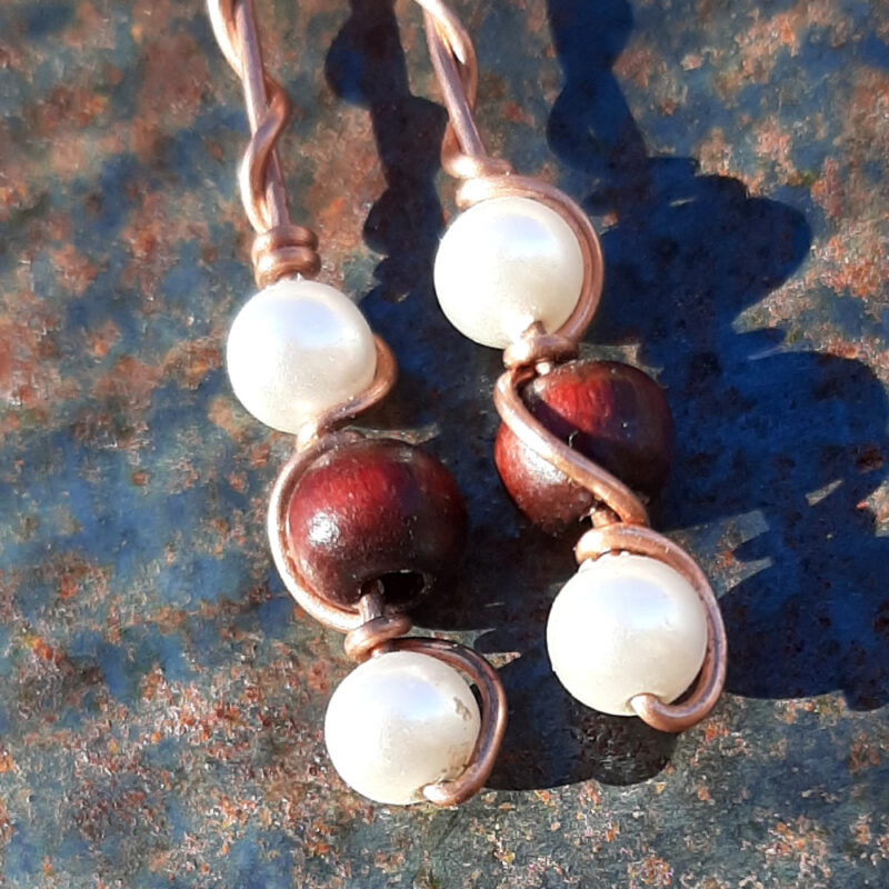 Each earring has a round red wooden bead with white beads above and below, all strung on copper wire that curves back up around each bead, then twists around itself.