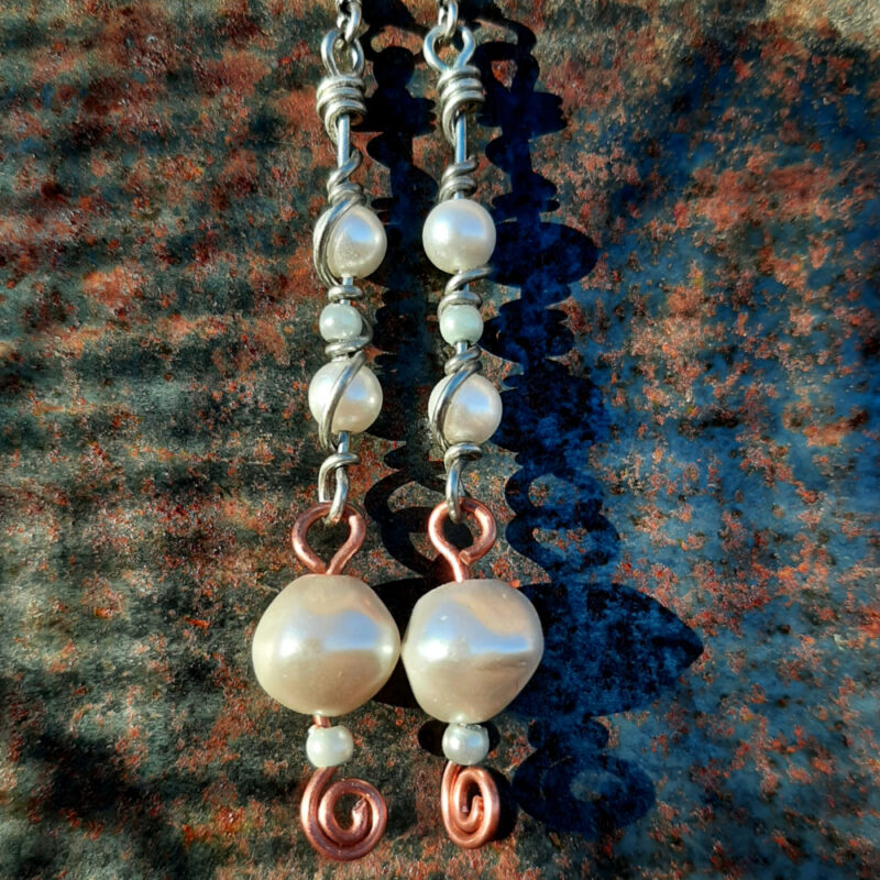 Copper and steel wire earrings, hinged at the middle; below, single white beads, each with a much smaller pale blue bead below; above, white and blue beads strung on steel wire that loops at the bottom and them winds back up and around each bead.
