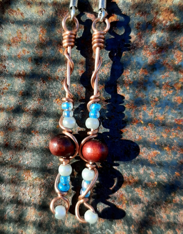 Each earring has a round red wooden bead with white and tiny blue beads above and below, all strung on copper wire that curves back up around each bead, then twists around itself.