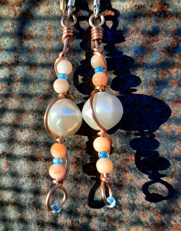 Each earring has a round white bead with peach and tiny blue beads above and below, all strung on copper wire that curves back up around each bead, then twists around itself.