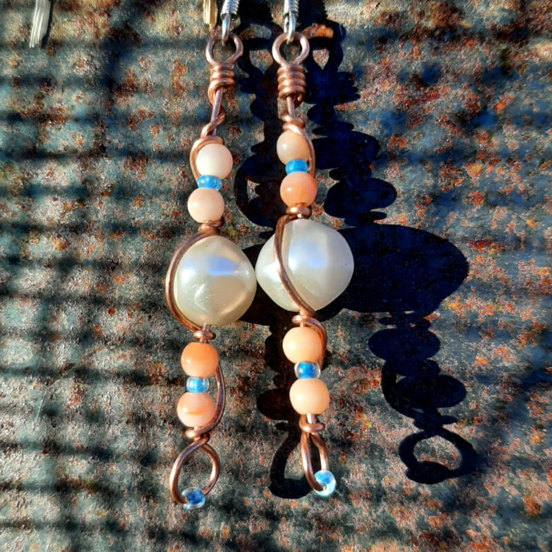 Each earring has a round white bead with peach and tiny blue beads above and below, all strung on copper wire that curves back up around each bead, then twists around itself.
