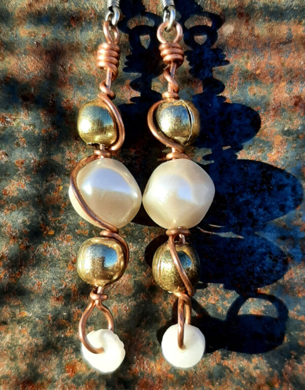 Each earring has a round white bead with brass beads above and below, all strung on copper wire that curves back up around each bead, then twists around itself.