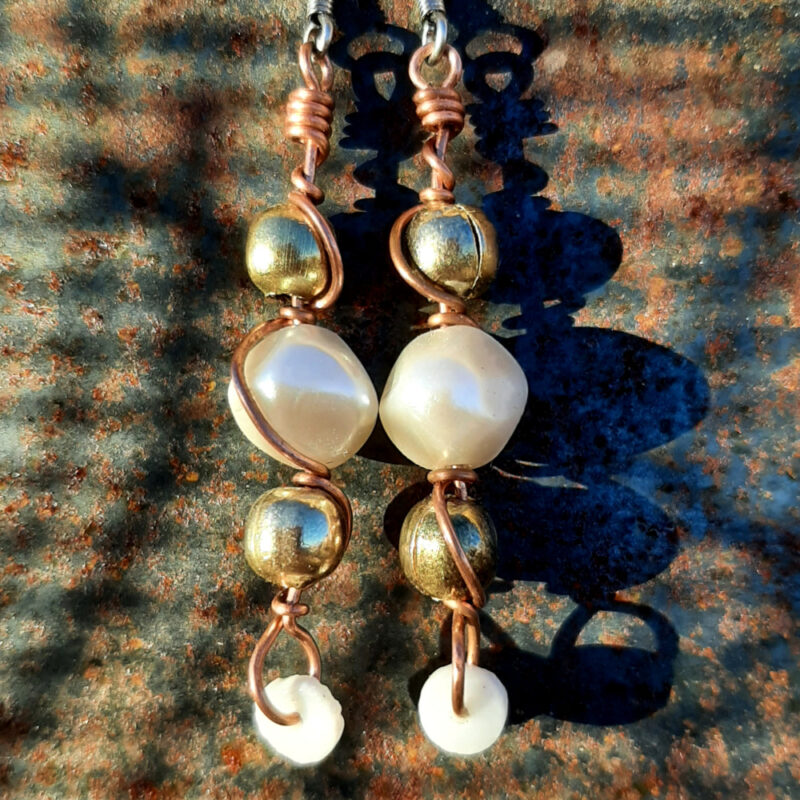 Each earring has a round white bead with brass beads above and below, all strung on copper wire that curves back up around each bead, then twists around itself.