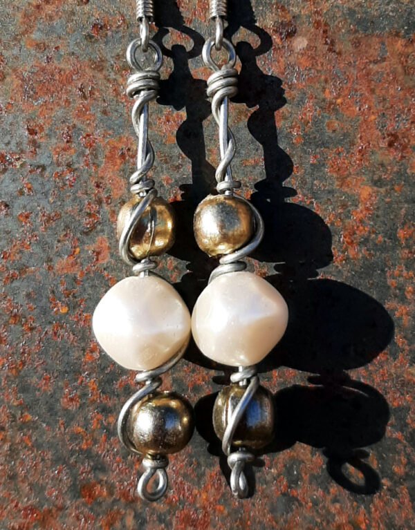 Each earring has two round brass beads to either side of a larger white bead, all strung on steel wire that curves back up around each bead, then twists around itself.