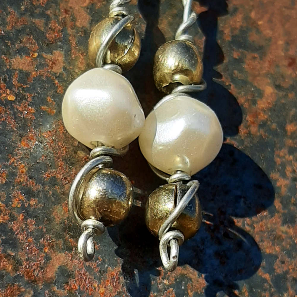 Each earring has two round brass beads to either side of a larger white bead, all strung on steel wire that curves back up around each bead, then twists around itself.