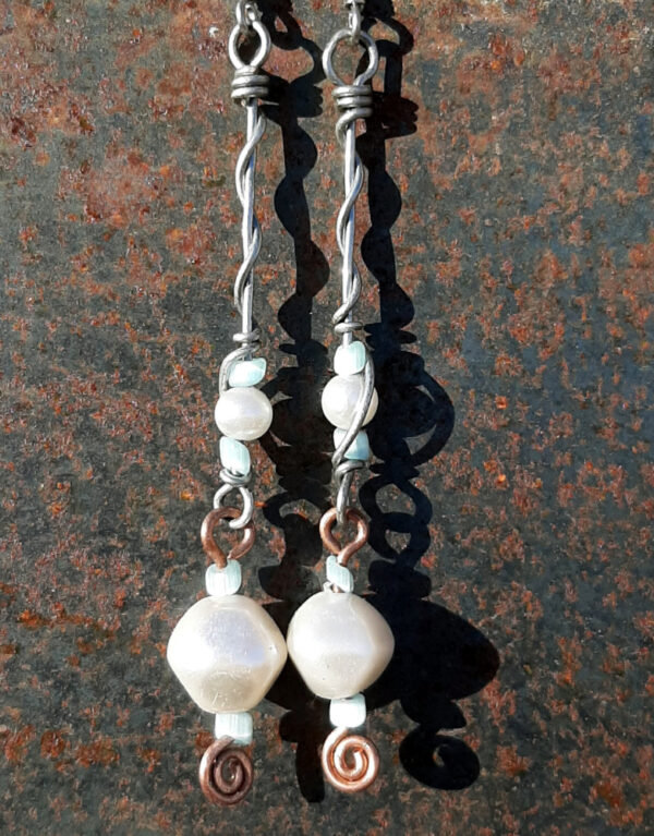 Each earring has two sections. The lower has a large white bead with a smaller pale blue bead above and below, all strung on copper wire with a neat spiral at the bottom. This is linked to a piece with pale blue beads above and below a white bead that's scarcely larger, all strung on steel wire that curves back up around each bead, then twists around itself.