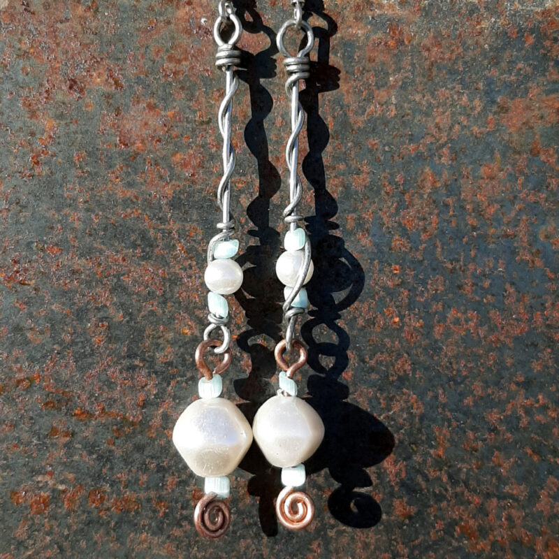 Each earring has two sections. The lower has a large white bead with a smaller pale blue bead above and below, all strung on copper wire with a neat spiral at the bottom. This is linked to a piece with pale blue beads above and below a white bead that's scarcely larger, all strung on steel wire that curves back up around each bead, then twists around itself.