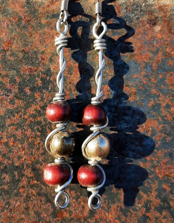 Each earring has a round brass bead with smaller round red wooden beads above and below, all strung on steel wire that curves back up around each bead, then twists around itself.