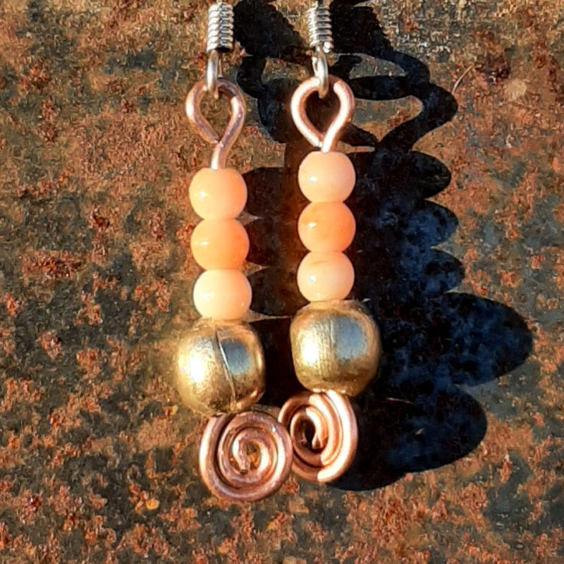 Each earring has a round brass bead below three round peach-colored beads. All are strung on copper wire that ends at the bottom in a neat spiral.