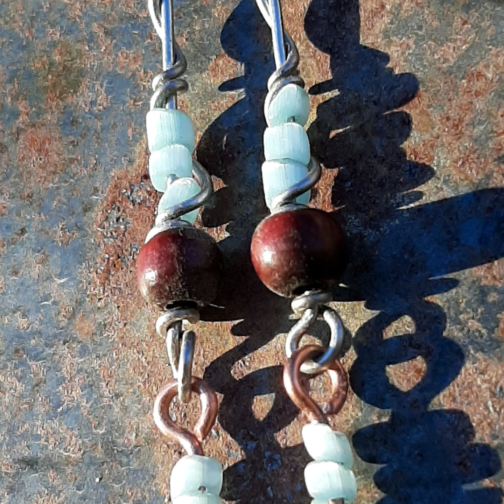 Each earring has two sections. The lower has three pale blue beads strung on copper wire with a neat spiral at the bottom. This is linked to a piece with pale blue beads above a round red wooden bead, all strung on steel wire that curves back up around each bead, then twists around itself.