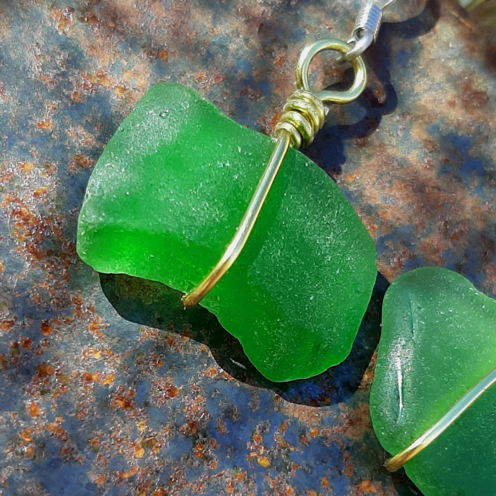 Each earring is a very roughly rectangular piece of green creek glass, simply wrapped in a single loop from top to bottom with gold-colored wire.
