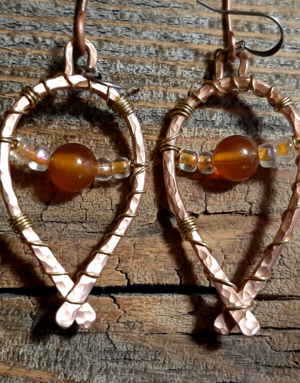 Each earring is hammered copper wire bent into a horseshoe shape, with brownish-orange beads draped across.