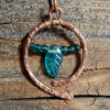 A hammered copper circle, almost, the ends not quite meeting at the bottom. Festooned across are teal green glass beads, a leaf between matching seed beads.
