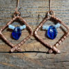 Each earring is a diamond shape of hammered copper wire, glass beads festooned within -- a cobalt blue leaf between white seed beads.