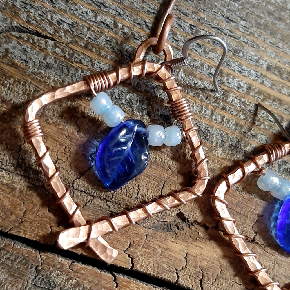 Each earring is a diamond shape of hammered copper wire, glass beads festooned within -- a cobalt blue leaf between white seed beads.