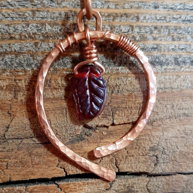 A hammered copper circle, almost, the ends not quite meeting at the bottom. A single red glass leaf dangles in the center.