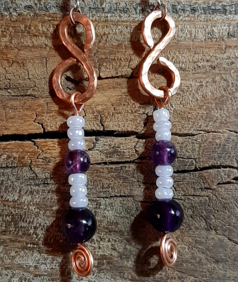 Each earring is an s-shaped piece of hammered copper wire, with strung white and purple beads dangling below.