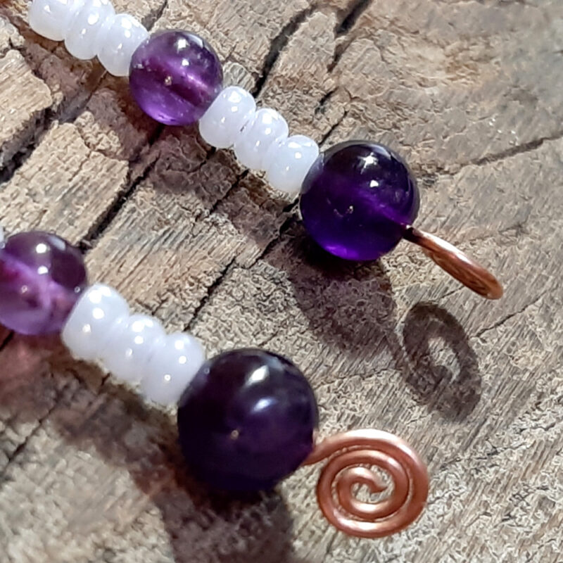Each earring is an s-shaped piece of hammered copper wire, with strung white and purple beads dangling below.