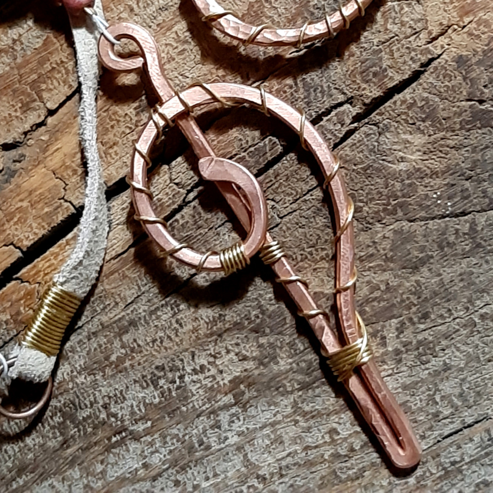 This pendulum starts at the top with a loop of hammered copper, and ends with more copper that crops straight down and then curves back up into a spiral. In between are a length of off-white leather thing, and grey-brown jasper strung with smaller brown beads.