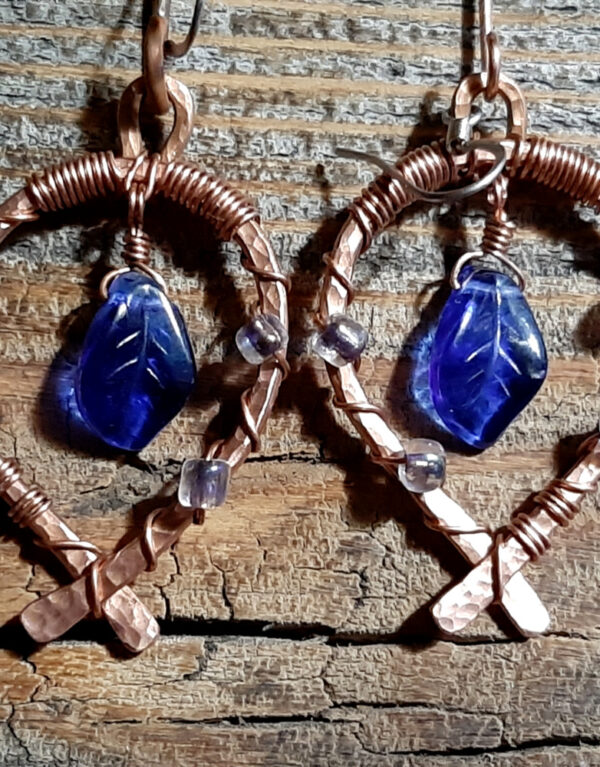 Each earring is hammered copper wire bent into a horseshoe shape, with clear glass beads wired onto it at intervals; in the center hang cobalt blue glass leaves.
