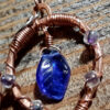 Each earring is hammered copper wire bent into a horseshoe shape, with clear glass beads wired onto it at intervals; in the center hang cobalt blue glass leaves.