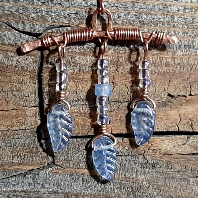 A gently arched piece of hammered copper wire, from which hang three frosted glass leaves strung on wire with small round clear beads.