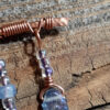 A gently arched piece of hammered copper wire, from which hang three frosted glass leaves strung on wire with small round clear beads.