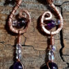 Each earring is hammered copper in a rough s shape, with amethyst and clear glass beads hanging below.