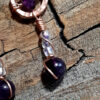 Each earring is hammered copper in a rough s shape, with amethyst and clear glass beads hanging below.