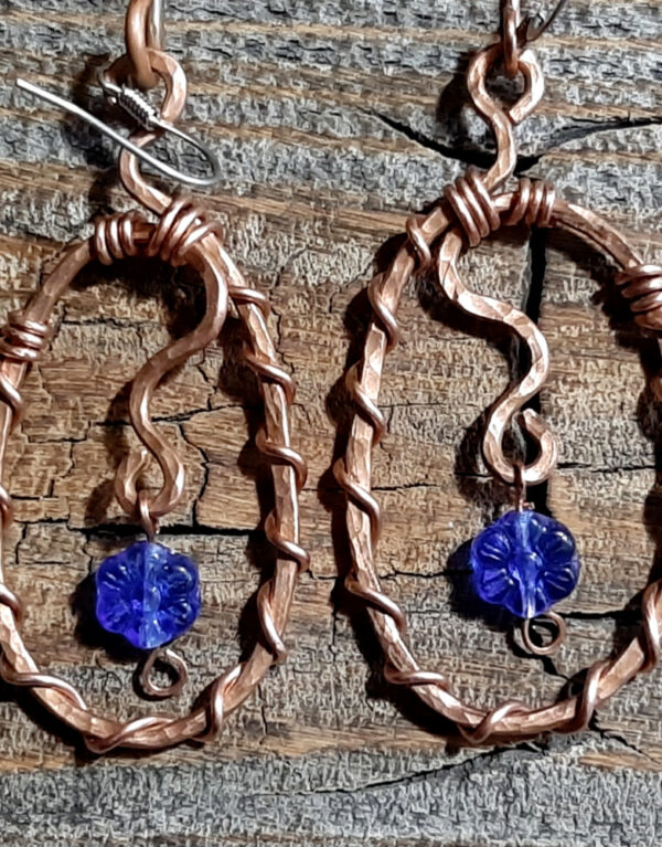 Each earring is an oval of hammered copper wire, with a flower-shaped cobalt blue glass bead suspended within.