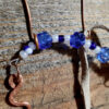 This pendulum features a squiggly pointer on one end and an oval finger loop on the other, both of hammered copper wire, with strung blue and white beads and a length of off-white leather thong in between.
