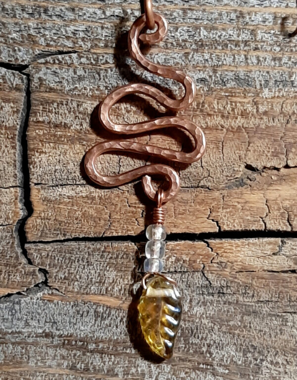 A squiggle of hammered copper wire; three small clear beads and a yellow glass leaf hang from the bottom.
