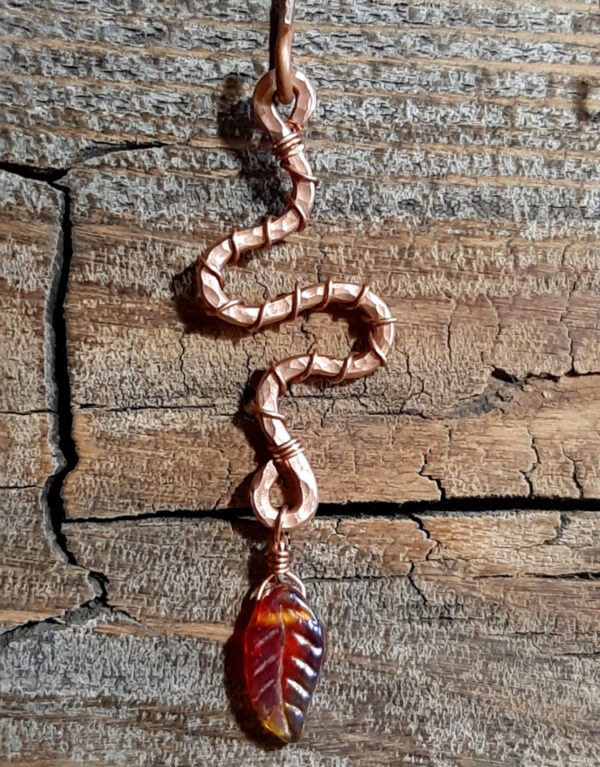 A squiggle of hammered copper wire; a rusty red glass leaf hangs from the bottom.