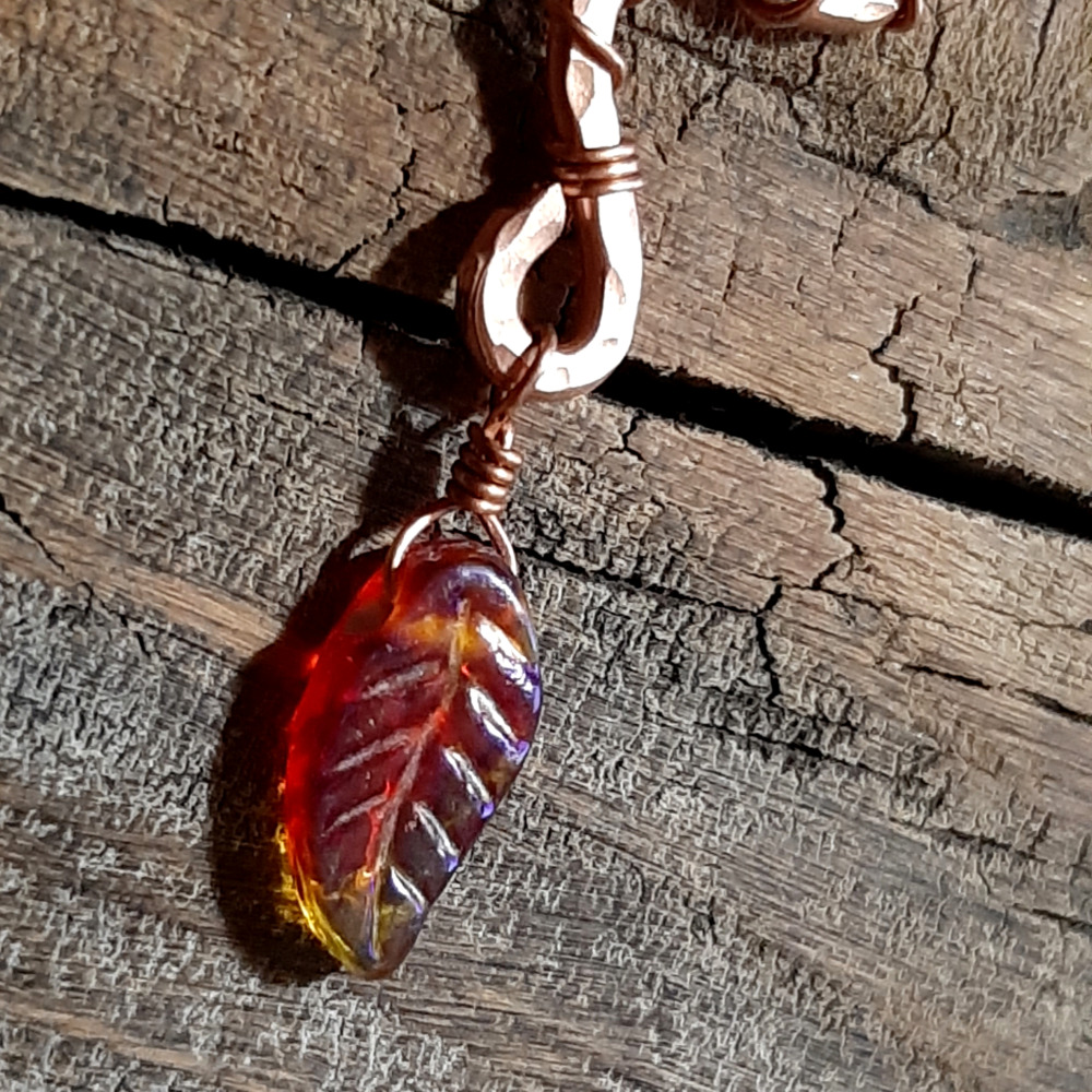 A squiggle of hammered copper wire; a rusty red glass leaf hangs from the bottom.