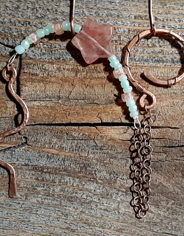 This pendulum has a simple squiggly pointer on one end and a rounded finger loop on the other, both made of hammered copper wire. In between is a length of copper link chain and some green and pink beads. One of the pink ones is a star.