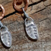 Each earring is a stylized S shape in hammered copper wire with a clear glass leaf hanging from the bottom.