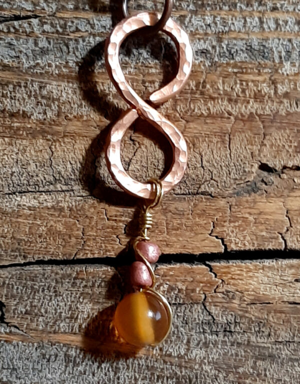 This pendant is a vertical infinity sign of hammered copper, with brown and amber-colored beads hanging below.